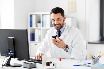 healthcare, medicine and people concept - happy smiling male doctor with drug in jar and computer at hospital