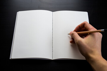 Blank sketchbook mock up on a desk. Male hands with pencil.