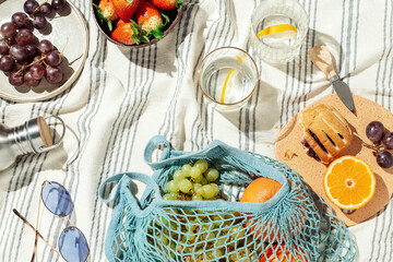 Summer picnic flatlay, fruits, berries and lemon water on striped cotton blanket