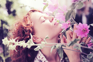 jeune et jolie jeune femme rousse caucasienne romantique aux longs cheveux bouclés souriant à pleines dents dans une nature entourée de fleurs roses 