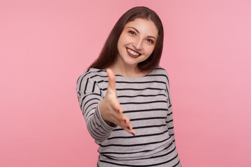 Fototapeta premium Welcome, nice to meet you! Portrait of happy amiable woman in striped sweatshirt giving hand to handshake and smiling friendly, greeting on job interview. studio shot isolated on pink background