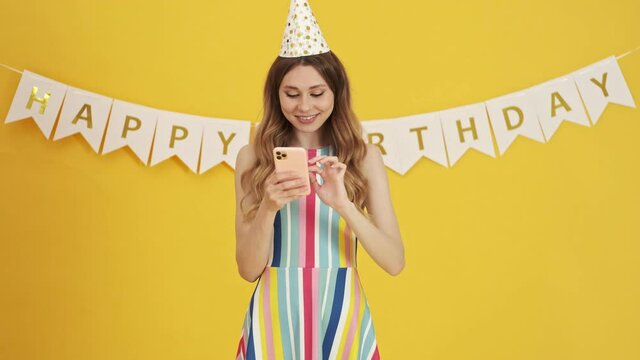 A pretty nice woman is using her smartphone on a birthday party isolated over a yellow background