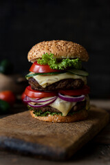 Hamburger with tomatoes, onions, cucumber, lettuce and melting cheese served on a  rustic wooden board 