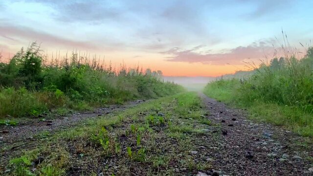 Sand road between foggy fields with beautiful sunset and colorful sky - Slow motion footage.