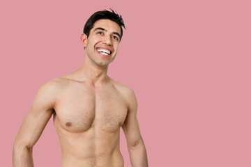 Fototapeta premium Young bare chested man smiling while looking away over pink background