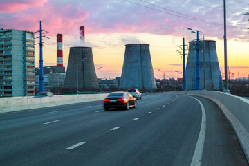 road with cars passing in succession with heat power plant at sunset in big city