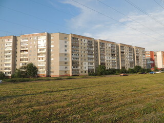 a typical Russian high rise building in the city against the background of a field with mown grass or lawn