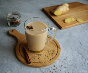 Traditional indian drink masala tea in a transparent glass mug on a wooden stand. Background gray, side view.