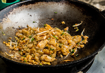 Frying noodles with chopped chicken in pan, Thai street food