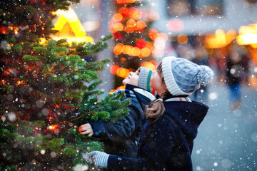 Two little kids, boy and girl having fun on traditional Christmas market during strong snowfall....