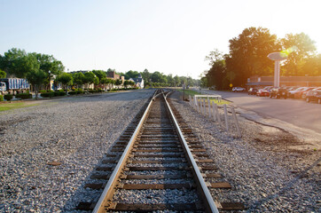 Fototapeta na wymiar A low level view of a single track freight railway line leading straight into the distance, on the the edge of a small South Carolina town. The sun has just risen giving an orange glow