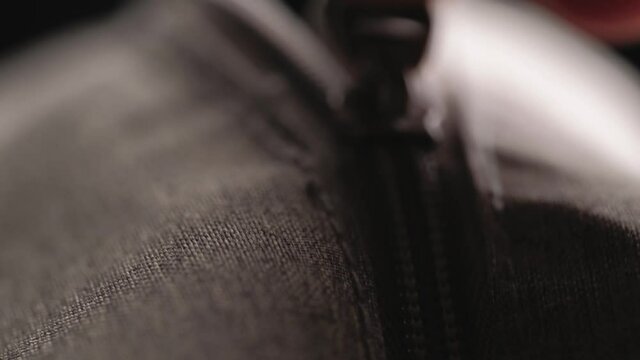 Close zipper with metal slider body with leather pull tab of gray cloth bag by hand in low light mood.
