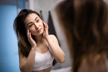 Young asian woman applies makeup in front of a bathroom mirror