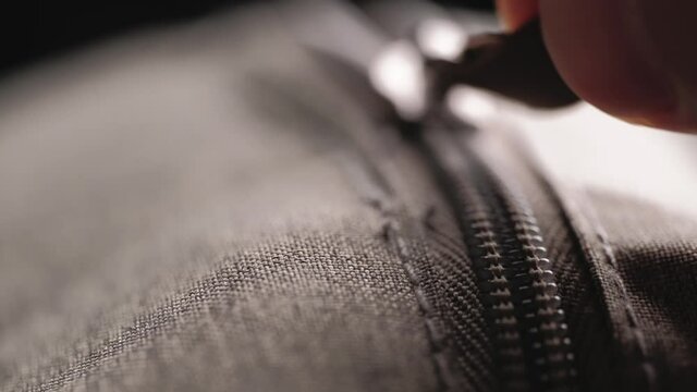 Open zipper with metal slider body with leather pull tab of gray cloth bag by hand in low light mood.