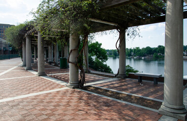 A section of the Augusta river walk with a shaded rest area under a pergola, with white columns. There is a view of the Savannah river. - obrazy, fototapety, plakaty