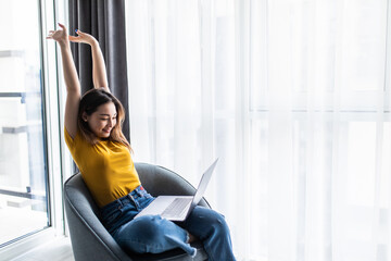 Happy relaxed casual woman sitting on the chair with a laptop in front of her stretching her arms above her head.