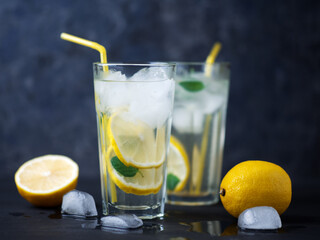 A glass of summer lemonade with lemon, mint, ice on a dark concrete table