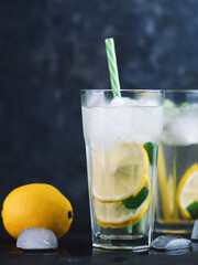 A glass of summer lemonade with lemon, mint, ice on a dark concrete table