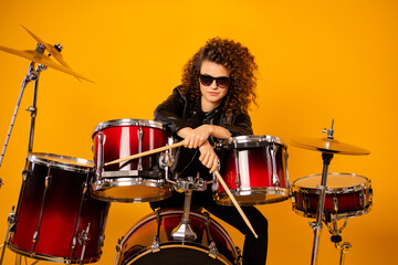 Fototapeta na wymiar Photo of popular rocker redhair cool lady plays instruments hold drum sticks posing photographer confident wear black leather outfit sun glasses isolated yellow background