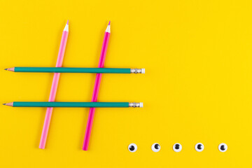 Hashtag sign from crossed colorful pencils on yellow background. Social media and creativity...