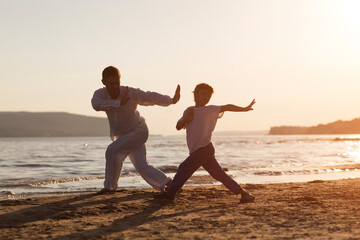 Family  dad and  son preschool child practice Tai Chi Chuan in the summer on the beach.  Chinese management skill Qi's energy. solo outdoor activities. Social Distancing. family exercising  together 