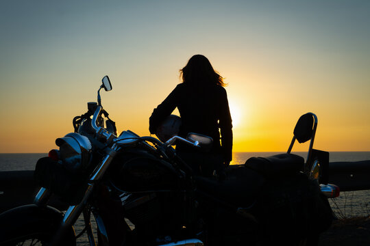 Girl and motorcycle silhouettes by the sea at dusk