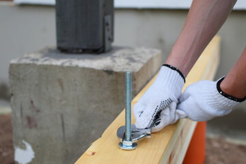 Gloved hand of worker tightens screw nut with adjustable metal wrench in wooden board construction...