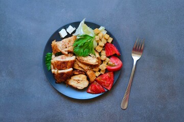 Pieces of baked chicken with tomato, cheese, crackers and herbs on a dark gray background. Top view.