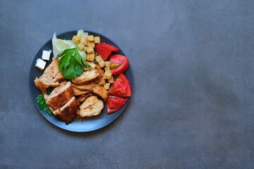 Pieces of baked chicken with tomato, cheese, crackers and herbs on a dark gray background. Top view.