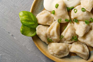 Fresh boiled meat dumplings served with sour cream on wooden background.