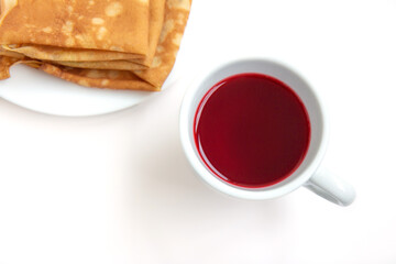 Red hibiscus tea in a white cup with pancakes on white background