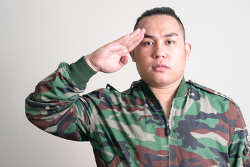 Young handsome overweight Asian man in military uniform saluting