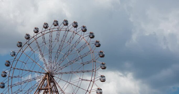 Big ferris wheel on blue sky and white clouds background in amusement park in city, timelapse video. Concept of leisure and rest on weekend. Big wheel on fun fair in entertainment park.