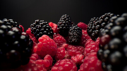 Close up of blackberries and raspberries fruits on plate and a black background. Fresh and tasty looking organic food for vegan in a summer season. Forest fruits.