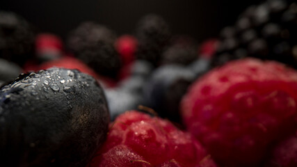 Close up view of fresh berries. Raspberries, blackberries and blueberries on black background. Tasty looking organic fruits covered with dew. 