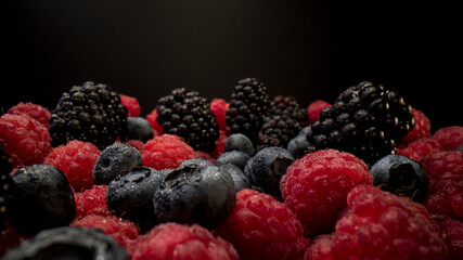 Close up view of fresh berries. Raspberries, blackberries and blueberries on black background. Tasty looking organic fruits covered with dew. 