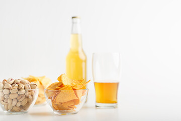 Pistachio, chips and nachos in plates. Glass of unfinished light beer and full bottle of lager