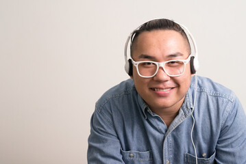 Happy young overweight Asian hipster businessman listening to music - obrazy, fototapety, plakaty