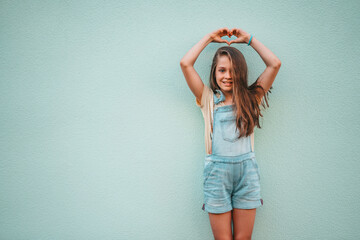 Portrait of a little girl child in a denim jumpsuit 9-13 years old on an empty wall, the girl shows...