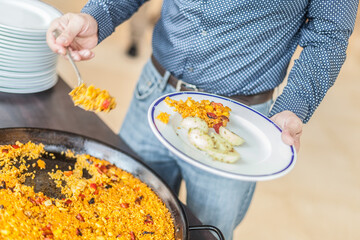 Un hombre con camisa y vaqueros se sirve un plato de paella valenciana en un buffet de un evento
