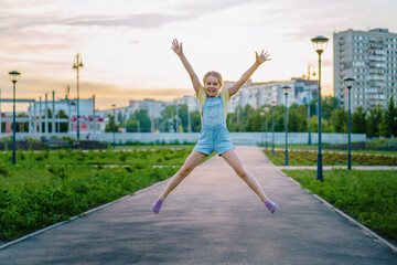 Fototapeta na wymiar Happiness, activity and the concept of a child-a smiling little girl in a denim jumpsuit jumps on the street