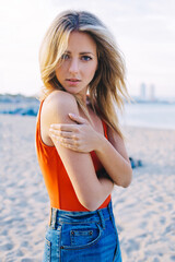 Portrait of a lovely young woman standing on the beach in summer, beautiful blonde hair female with slender figure posing for the camera at sunny afternoon at seashore outdoors