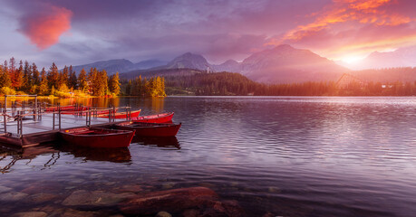 Fototapeta premium A wonderful Colorful Sunset at lake Strbske pleso, in High Tatra. Picturesque Dramatic sky glowing in sunlight, over the Fairytale calm lake. Scenic image of woodland in sunlit. Autumn Landscape.