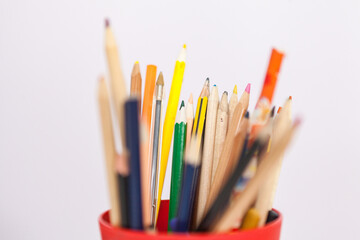 Un puñado de lápices con diferentes tamaños y colores dentro de un vaso de plástico.