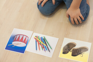 Un niño de rodillas observa unas fotografías a modo de fichas de logopedia.