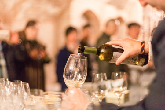 Una mano con una botella de vino blanco sirviendo en una copa de vino