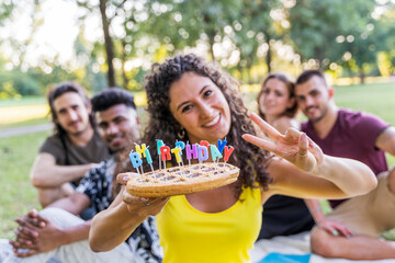 multiethnic group of millennial friends celebrating a birthday with a cake outdoors