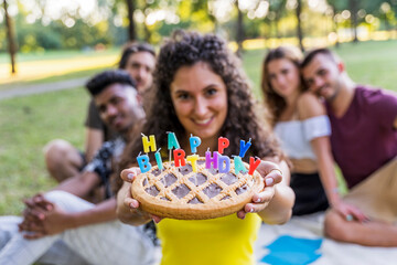 multiethnic group of millennial friends celebrating a birthday with a cake outdoors