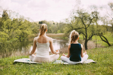 Mother and daughter sit in the Lotus position in the garden. The family practices yoga outdoors....