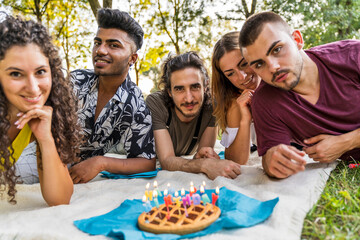 multiethnic group of millennial friends celebrating a birthday with a cake outdoors